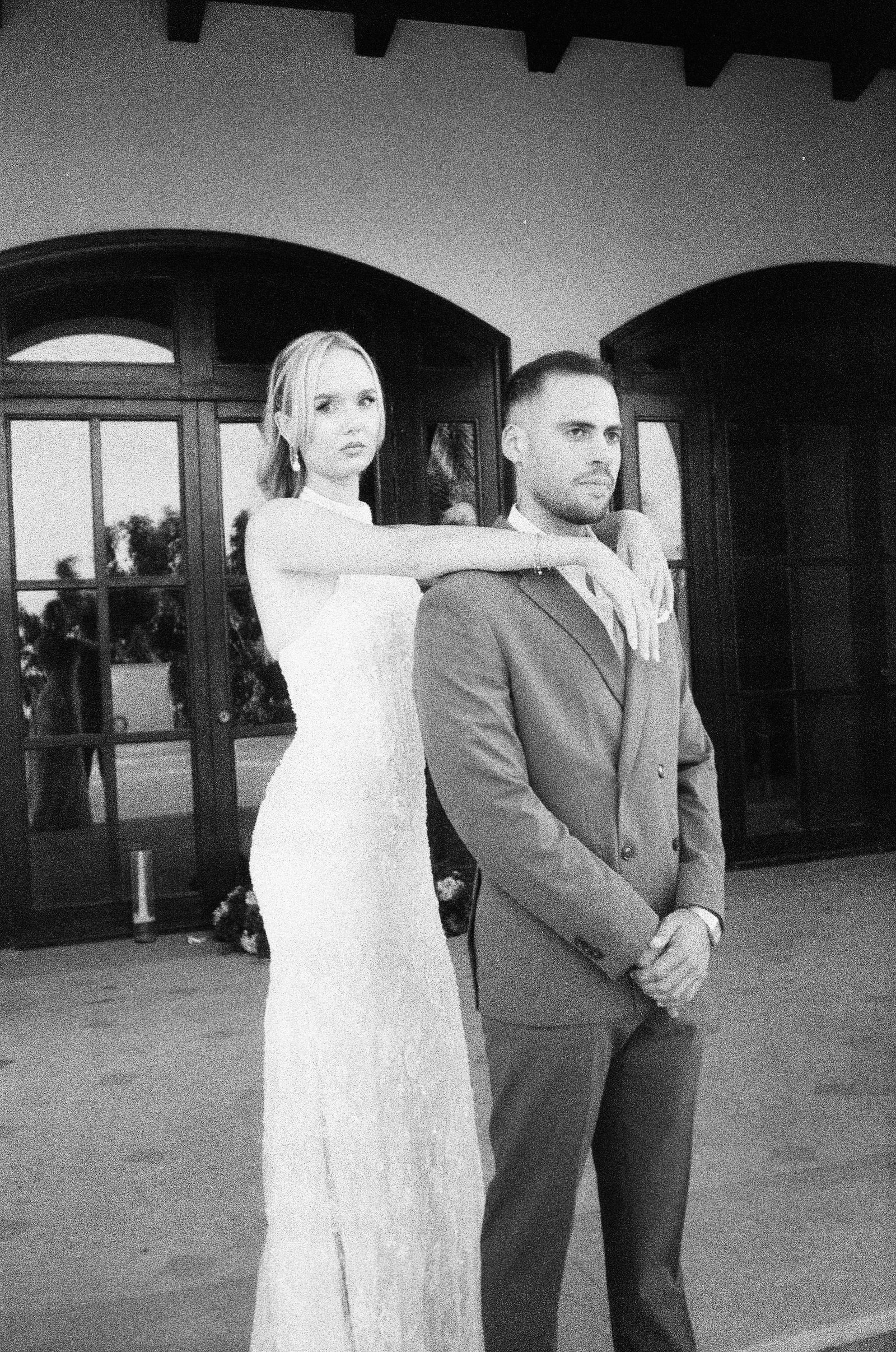 Bride and groom standing close in front of arched doors, black and white