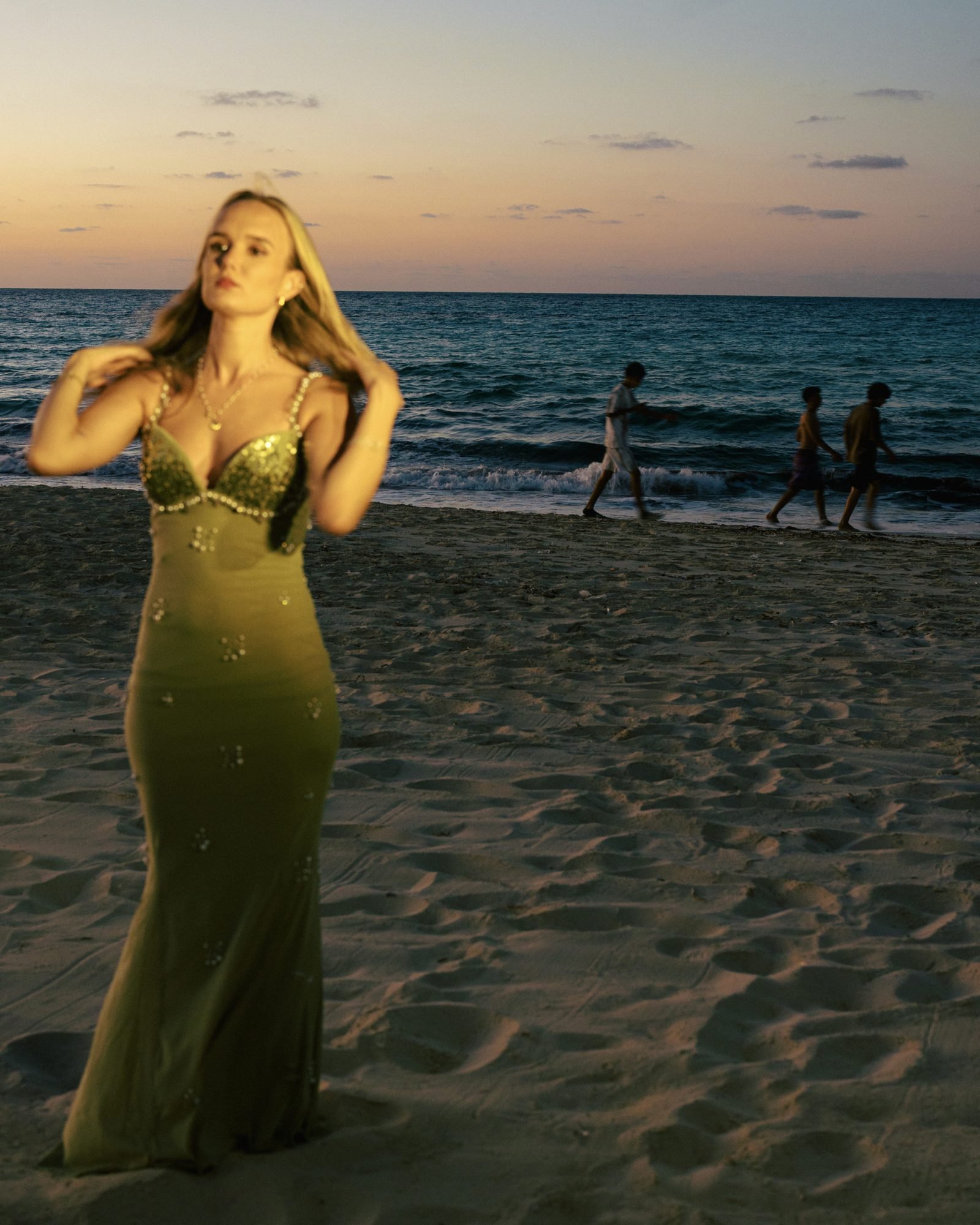 Woman in an olive beaded gown on the beach at dusk