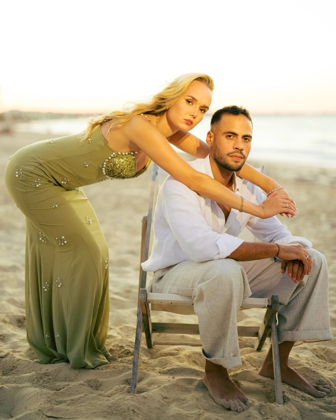 Woman in an olive gown leaning over a man seated on a beach chair