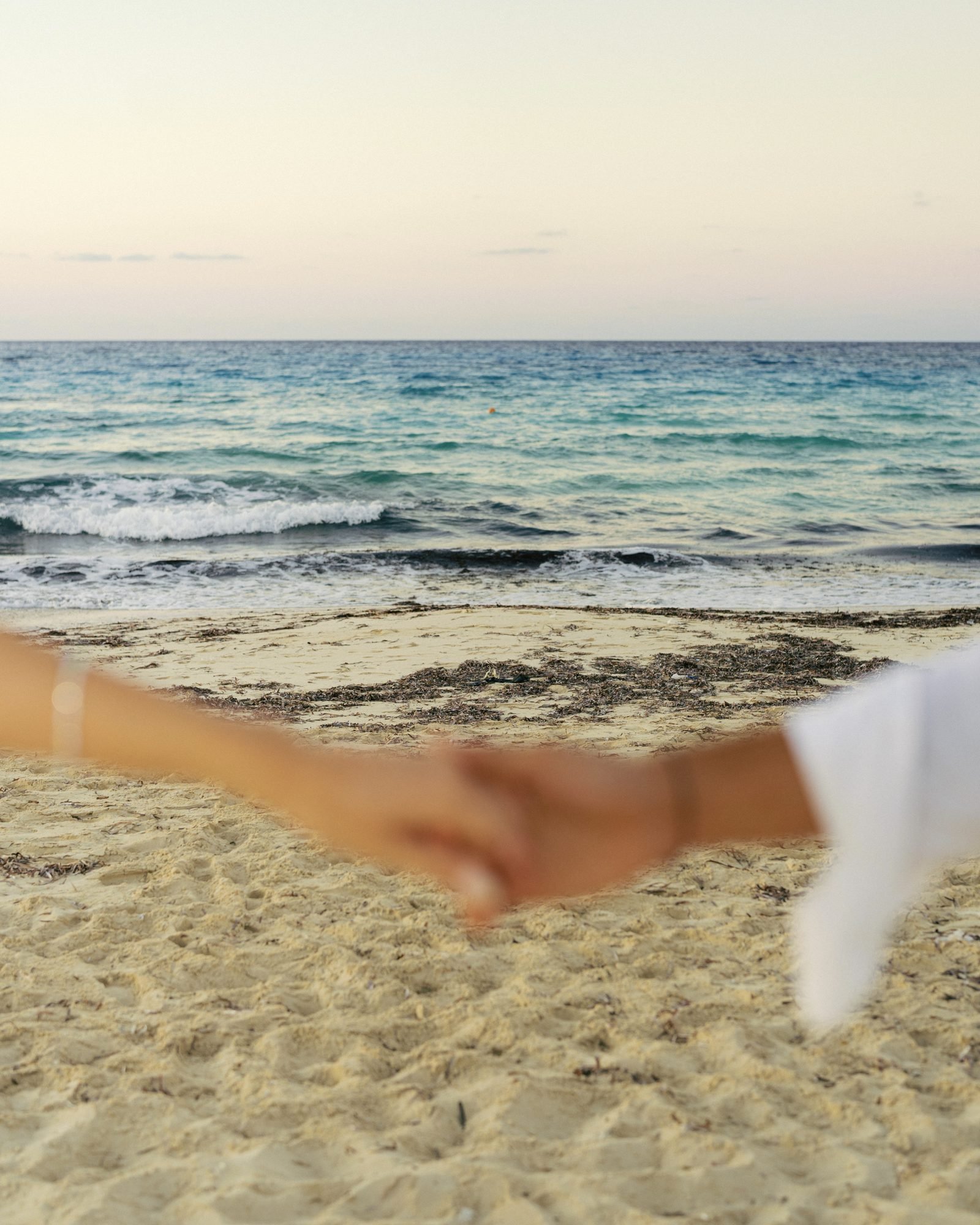 Two hands reaching for each other on the sand by the sea