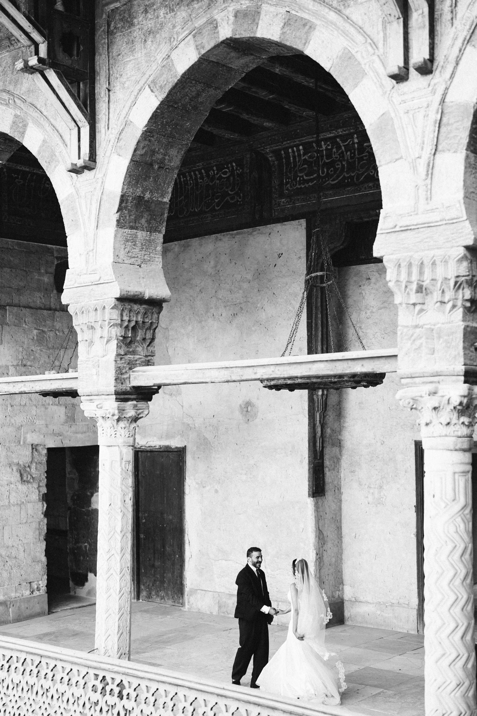 Bride and groom beneath stone arches, black and white