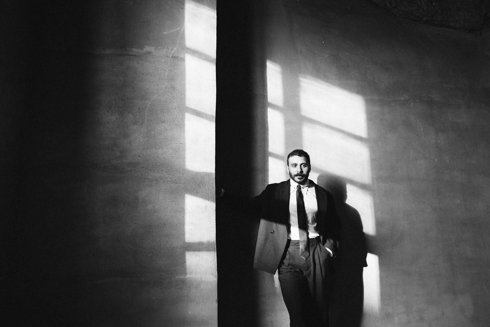 Groom standing in a doorway of light and shadow, black and white
