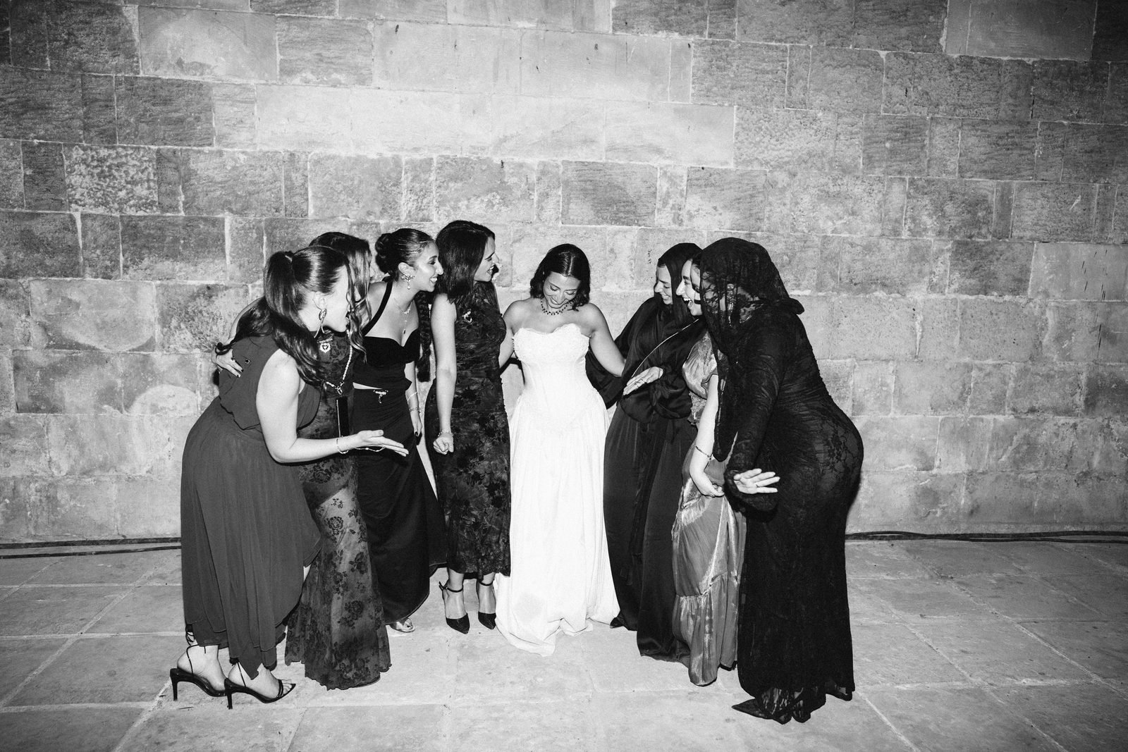 Bride laughing with her friends against an old stone wall, black and white