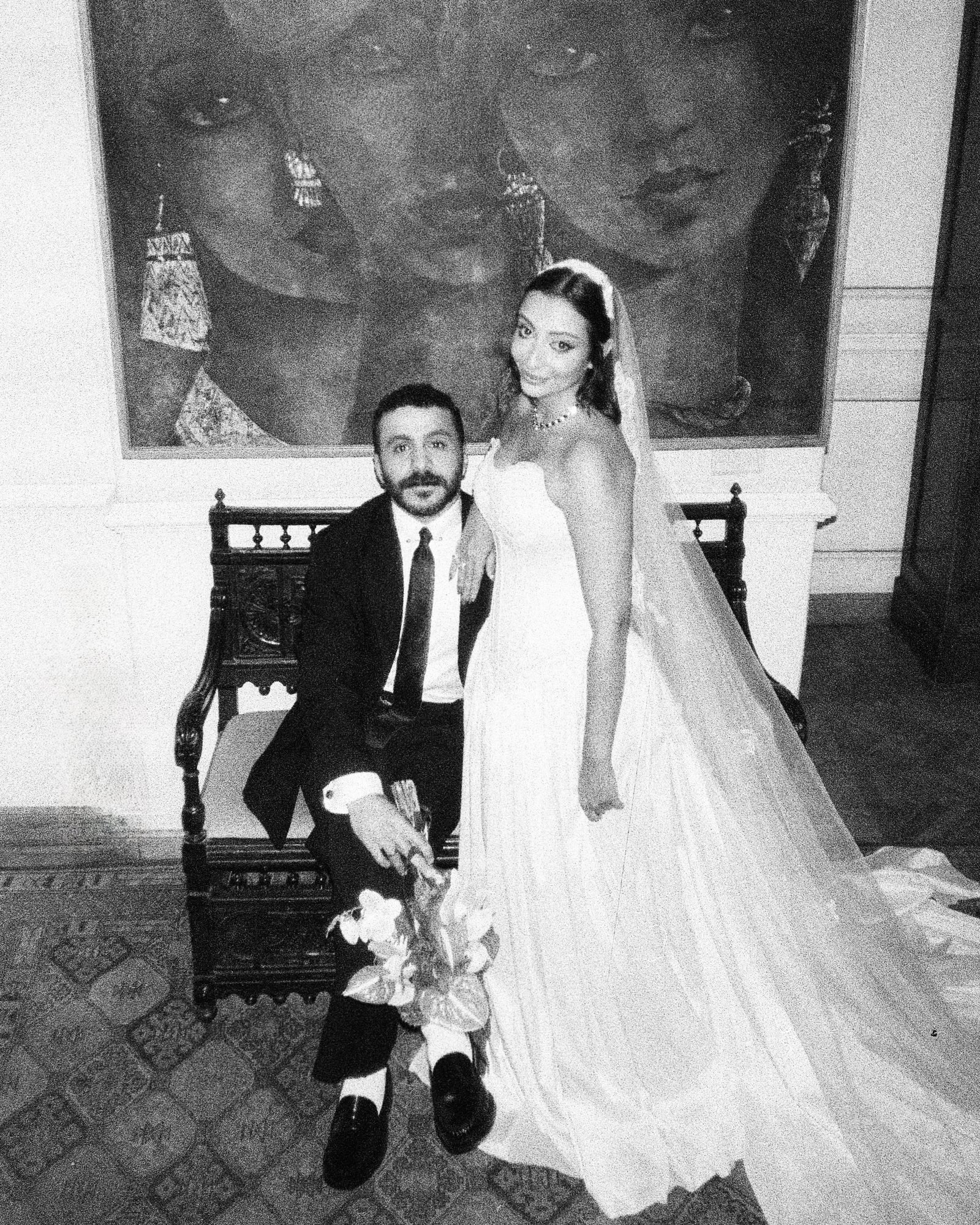Groom and bride seated together in a carved chair, black and white