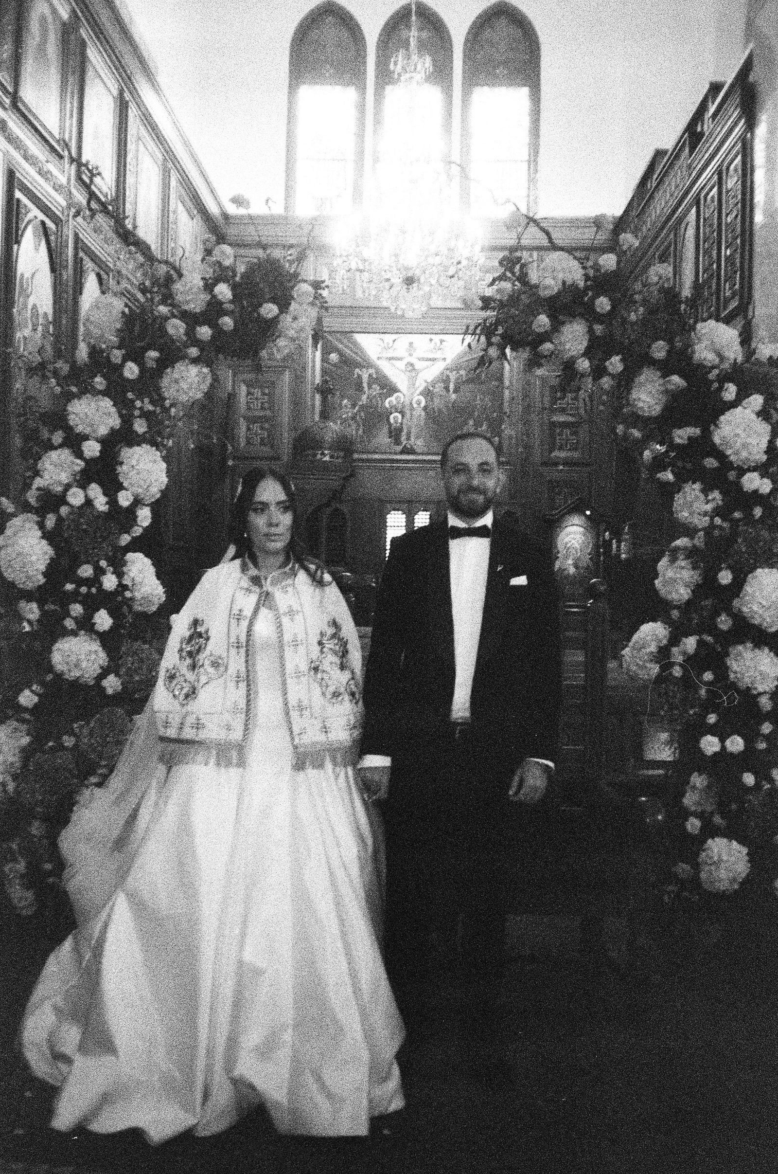 Bride and groom in front of a floral arch, black and white