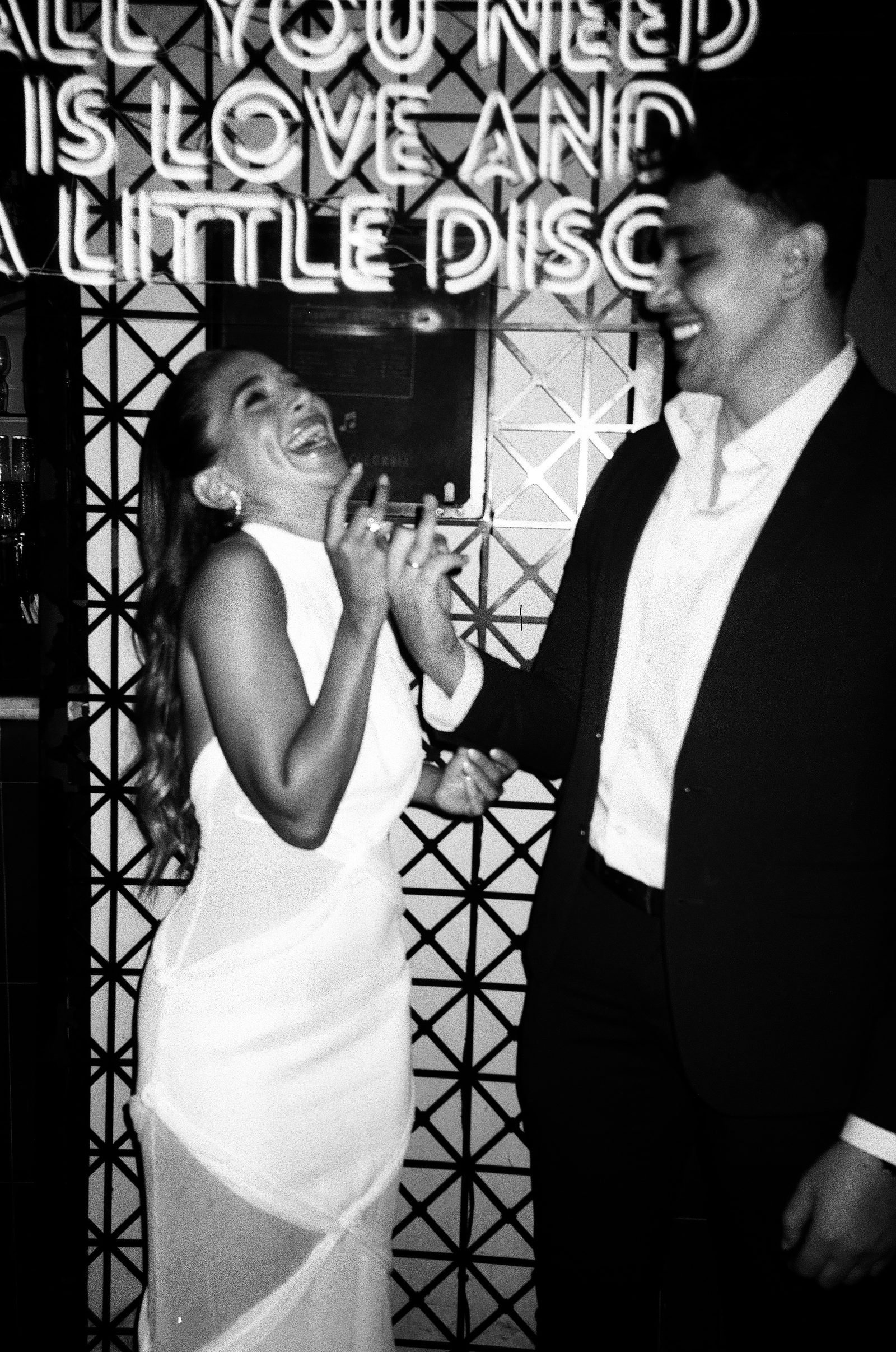 Couple laughing beside a neon sign, black and white