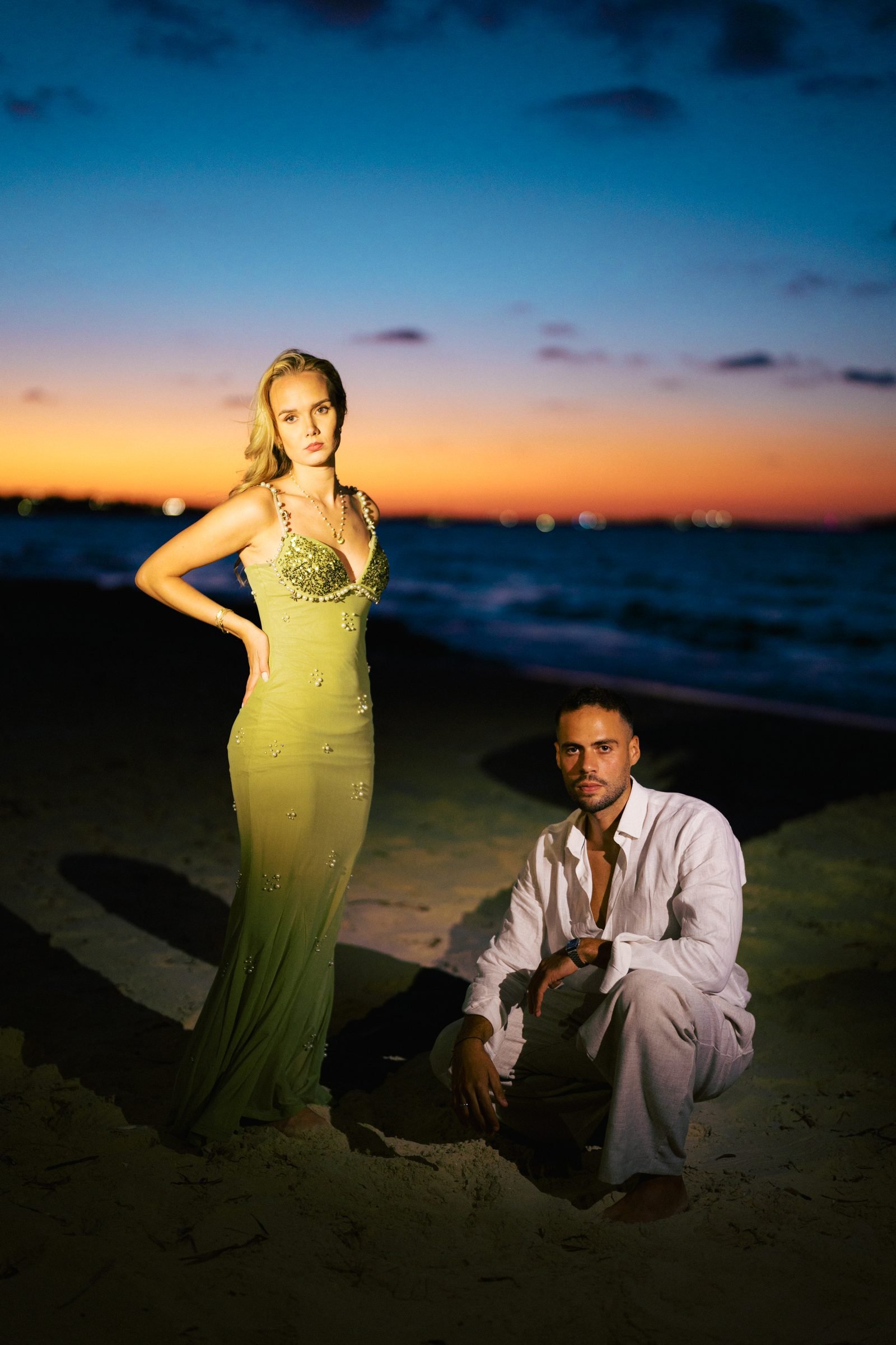 Woman in a green gown and man on the beach at twilight