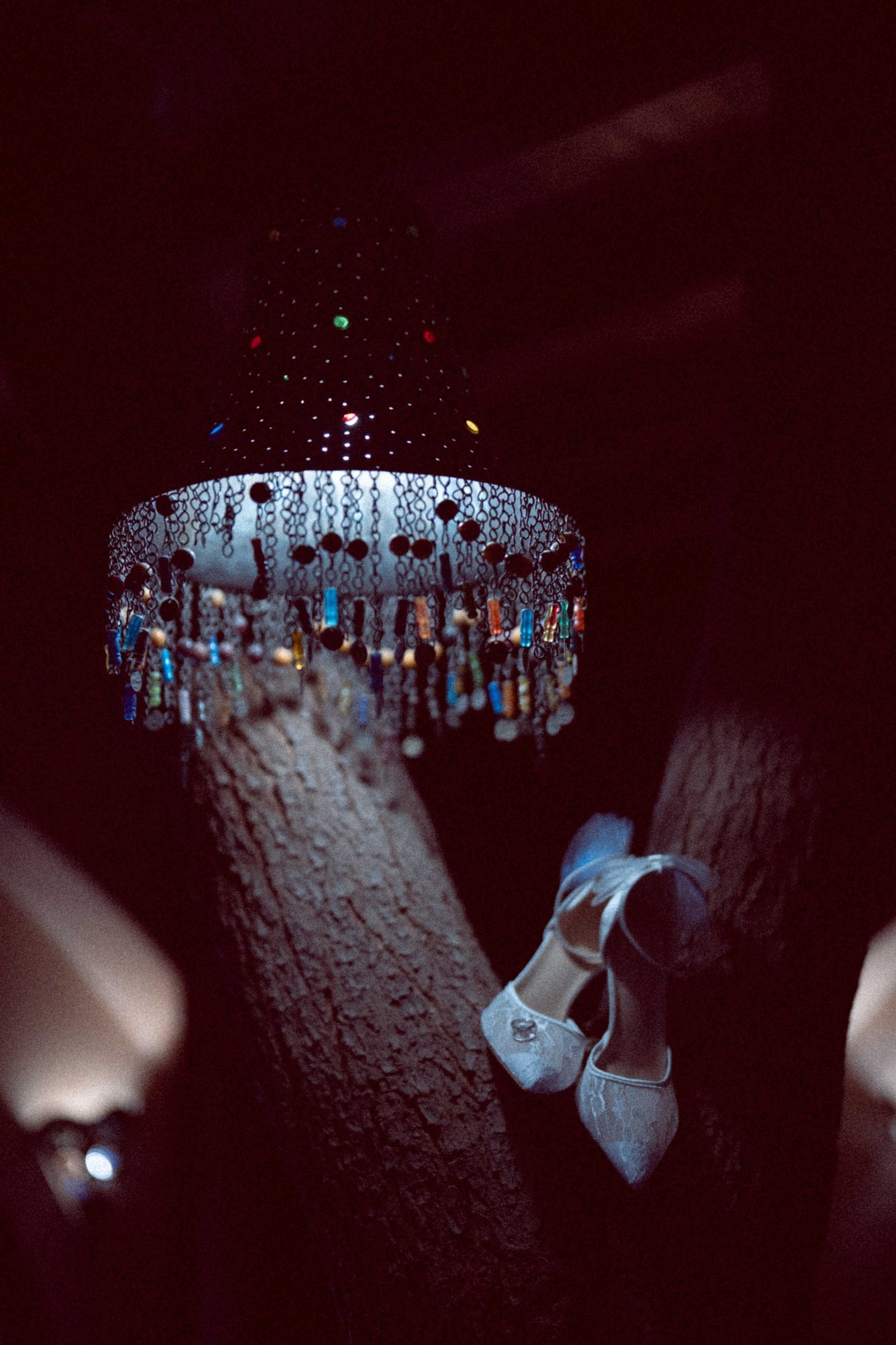 Crystal chandelier above a tree trunk with bridal shoes resting below