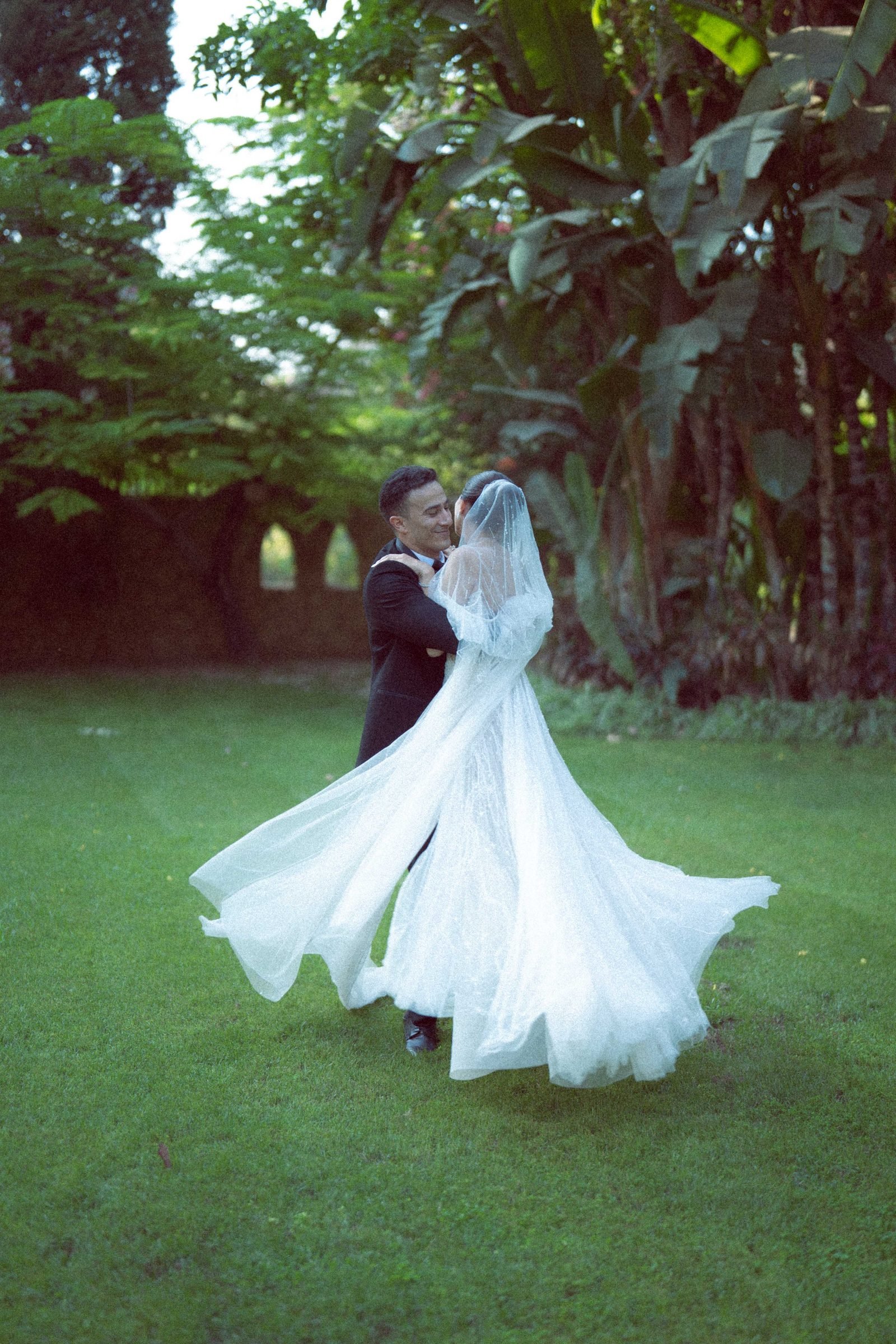 Bride twirling in a flowing gown on a lawn beside the groom