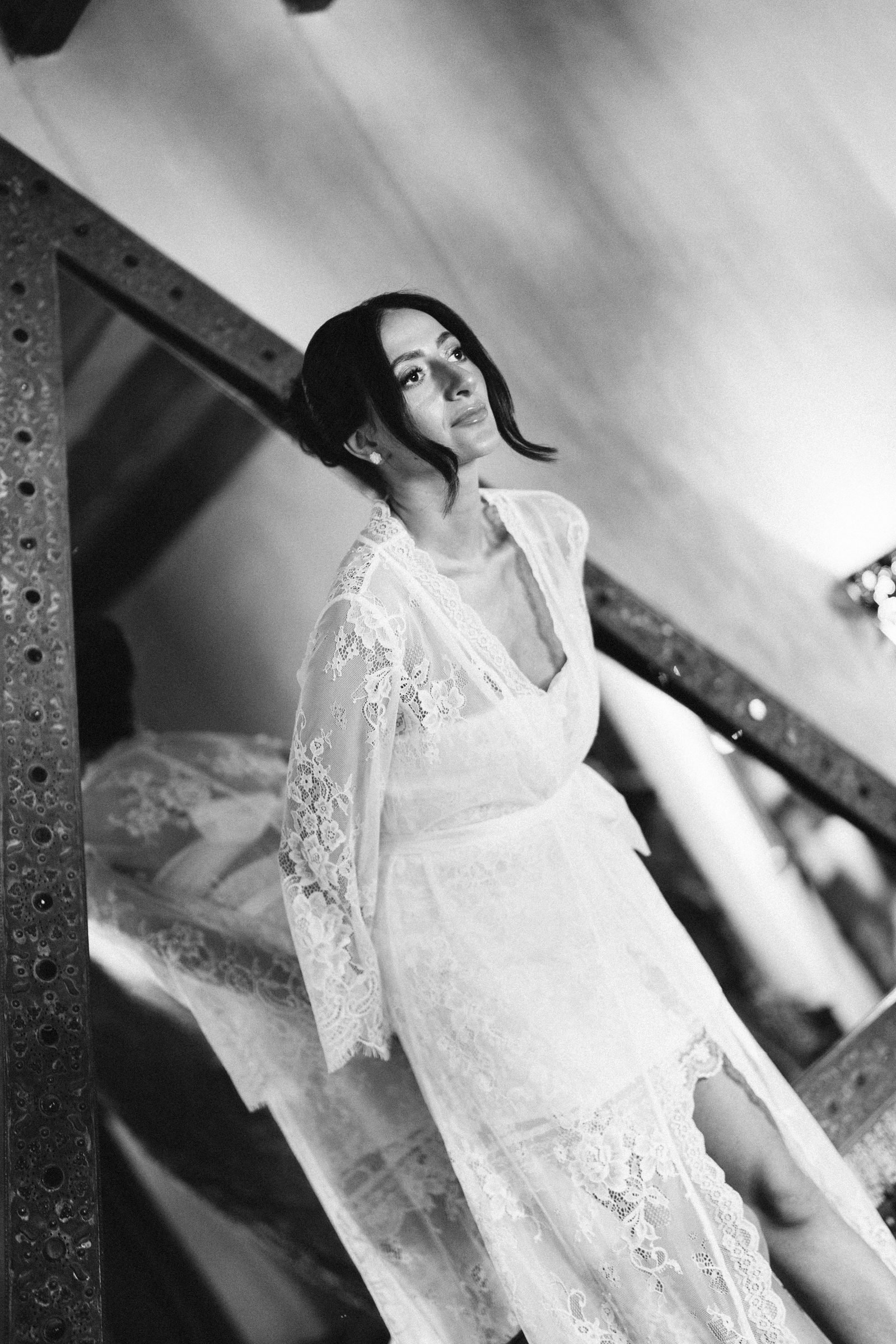 Bride in a lace robe leaning against an iron frame, black and white