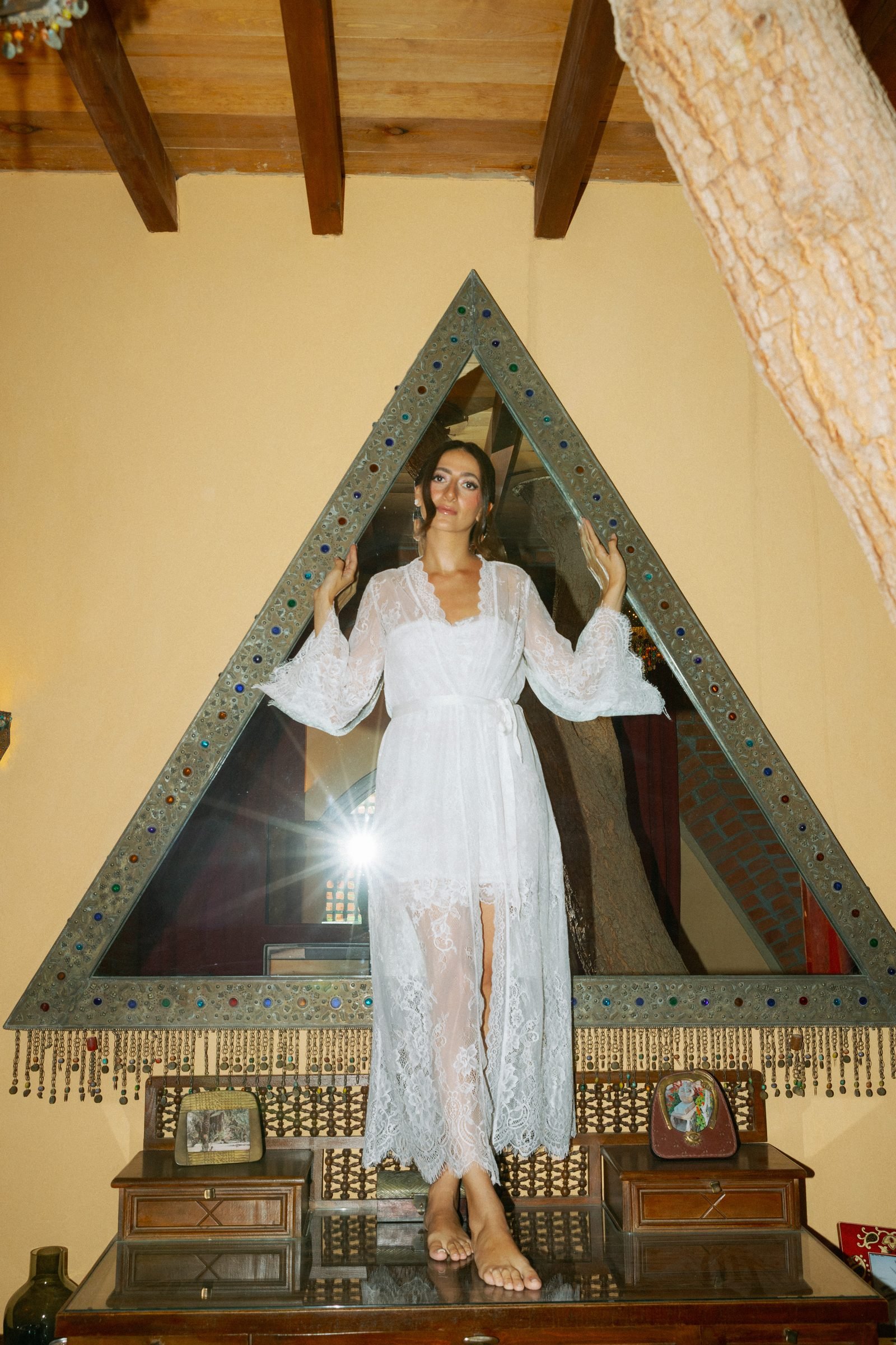 Bride in a lace robe standing inside a triangular mirror frame