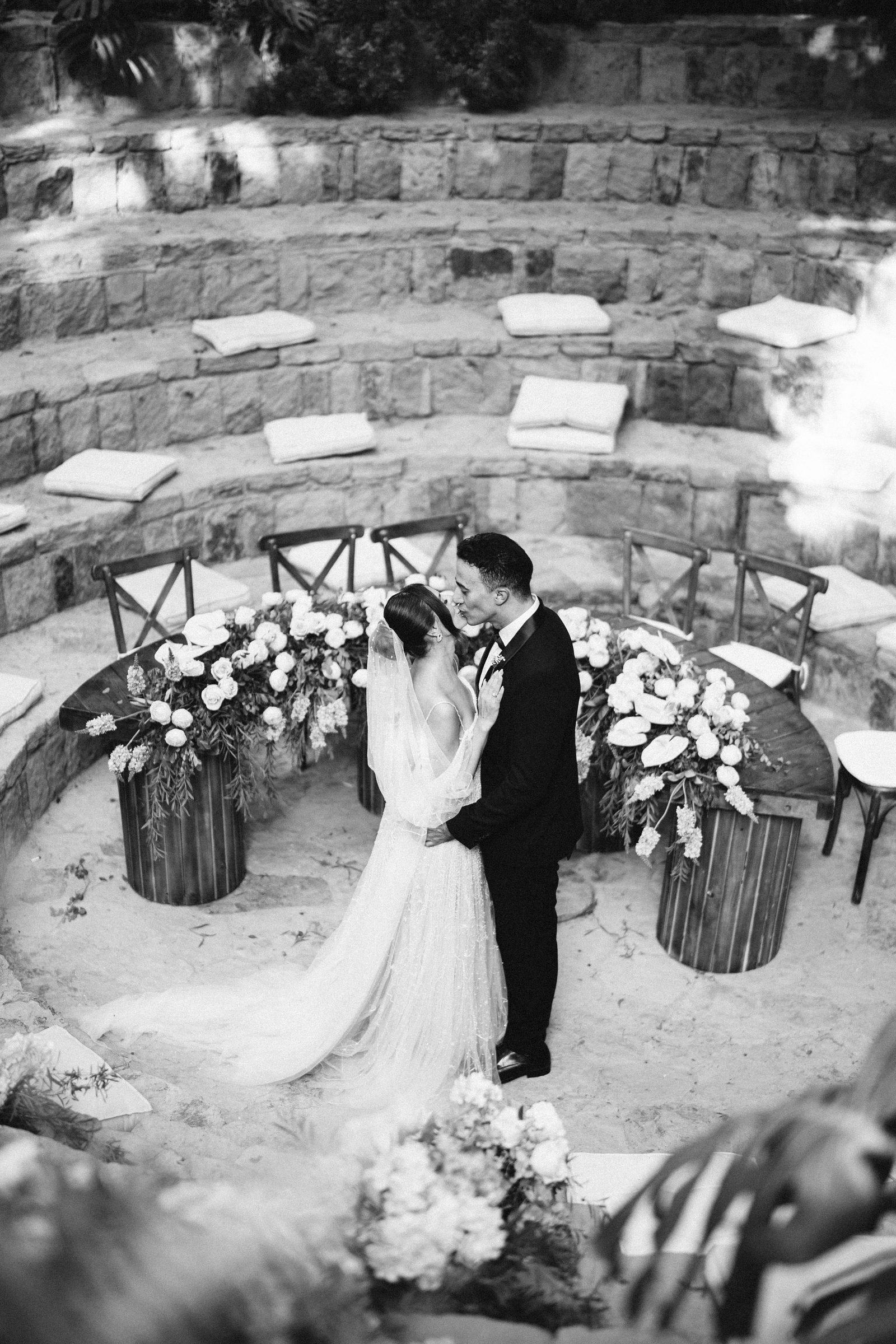 Couple kissing in a circular stone garden ringed with flowers, black and white