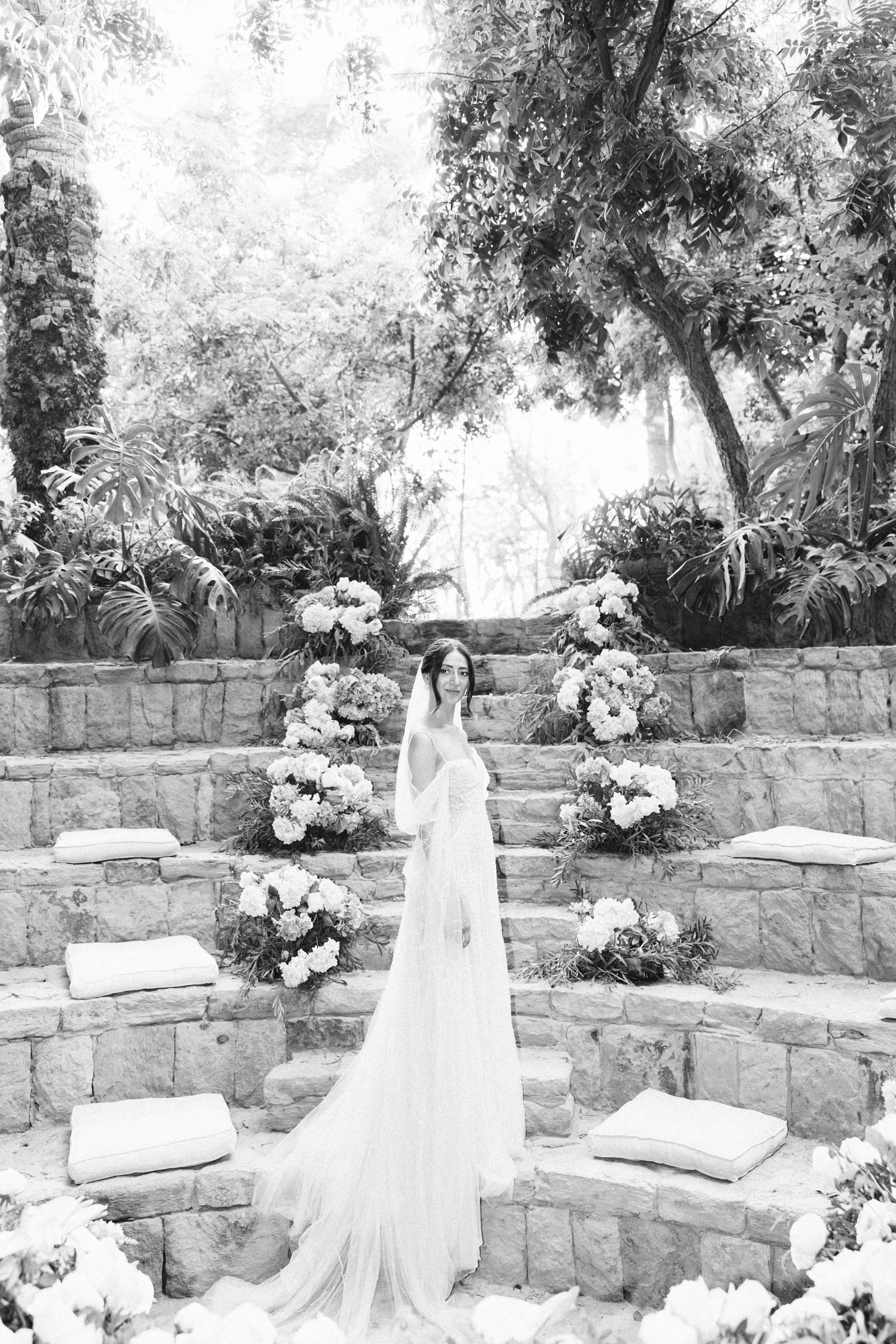 Bride standing on stone steps lined with flowers, black and white