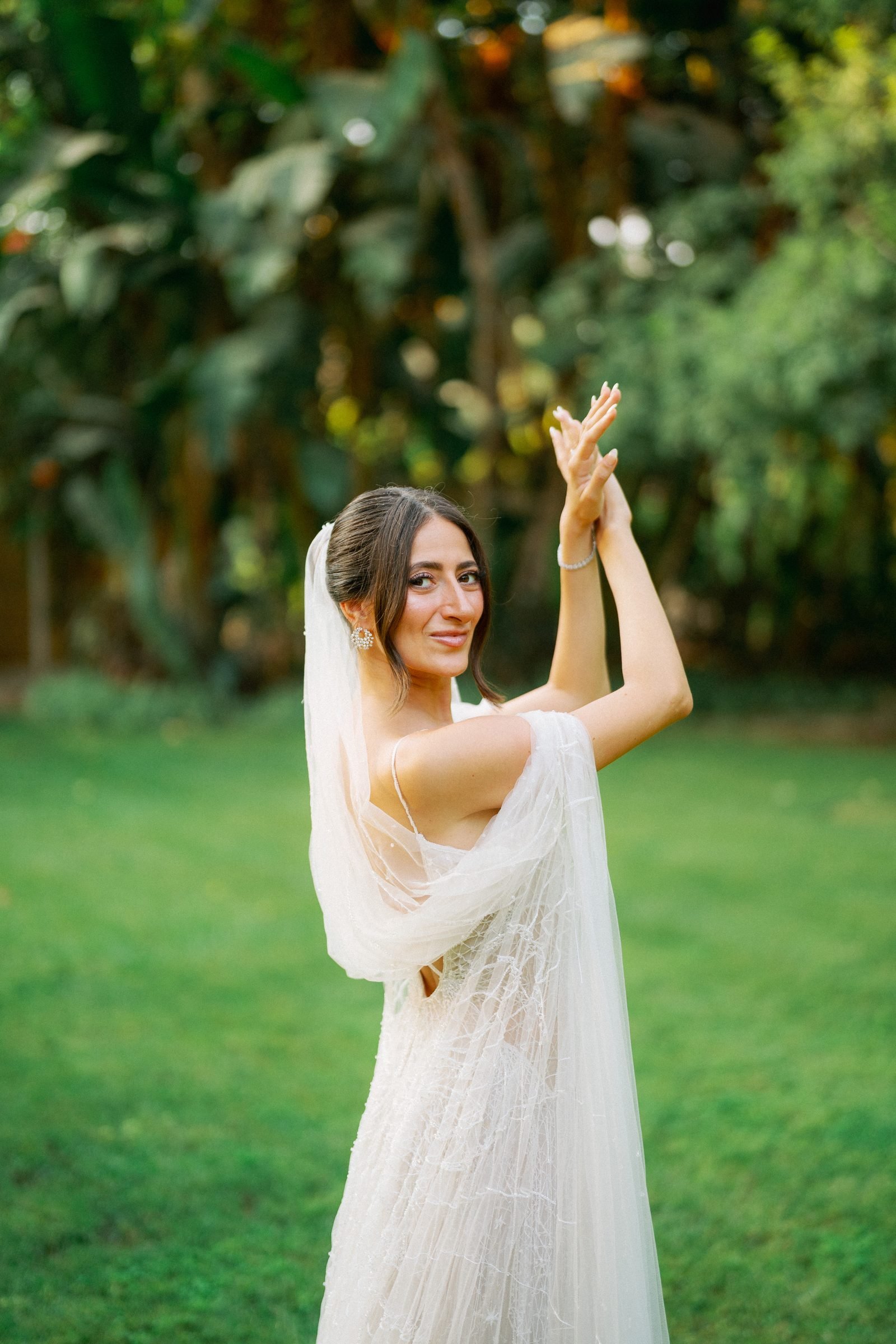 Bride in a veil raising her arms on a lawn
