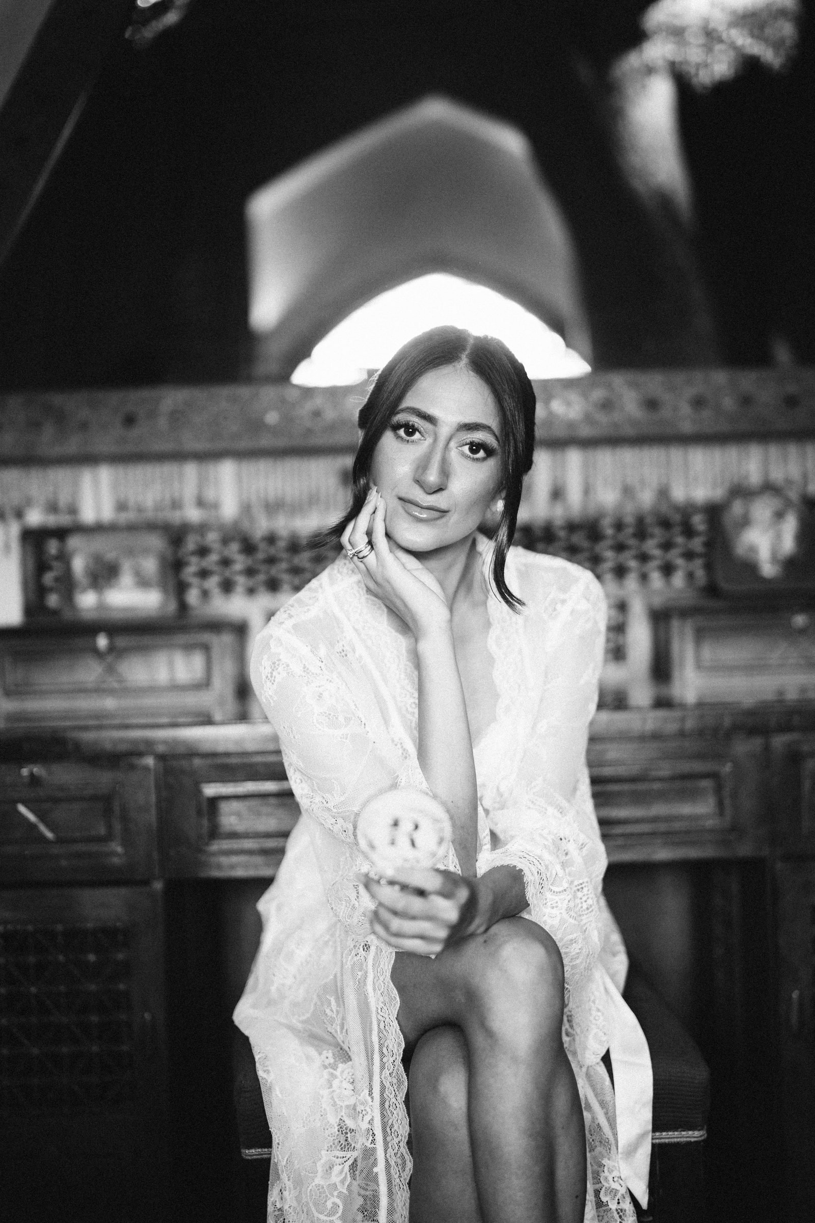 Bride in a lace robe seated in front of carved wood, black and white